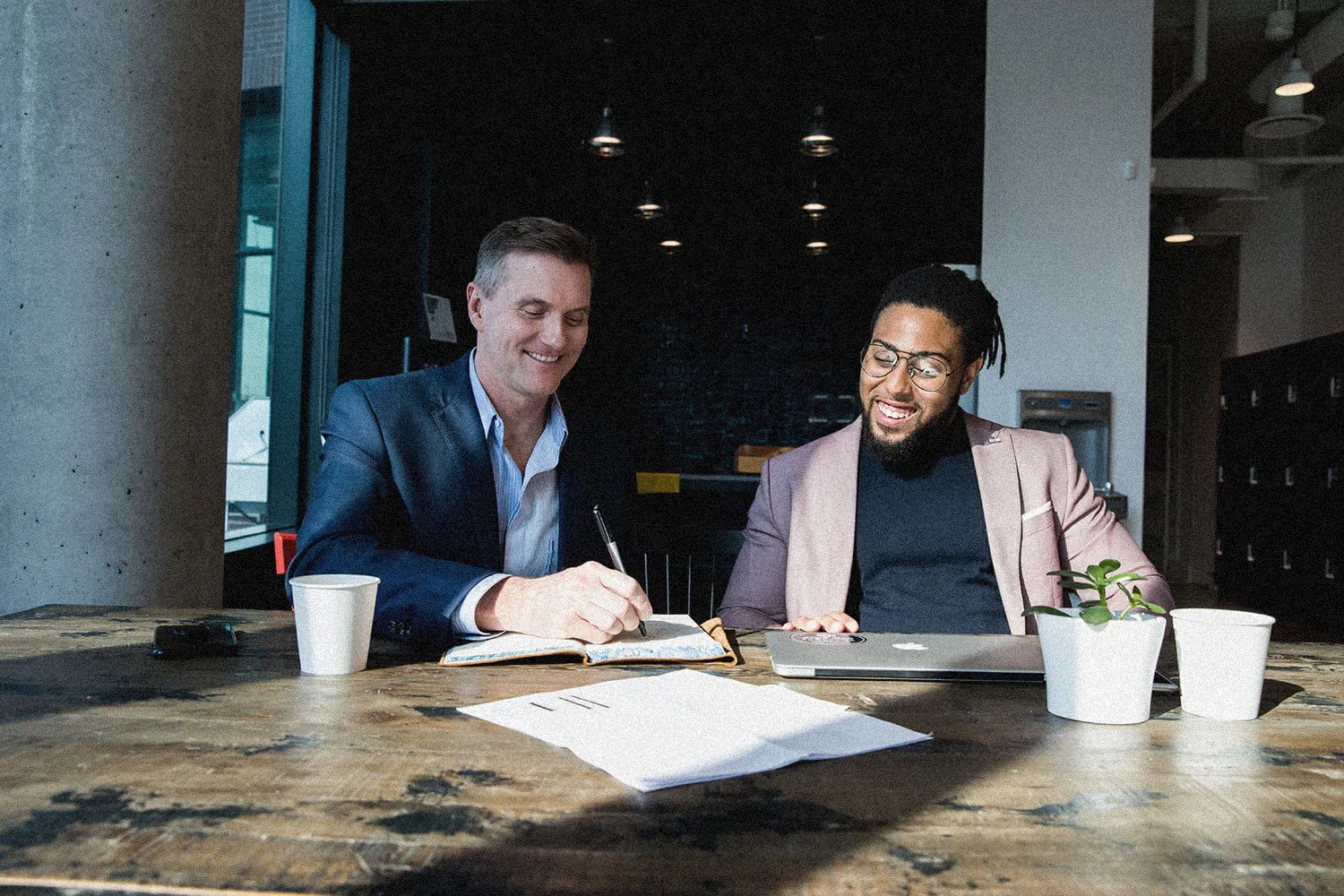 Overhead of hands, coffee, and an open laptop on a weathered wood surface.