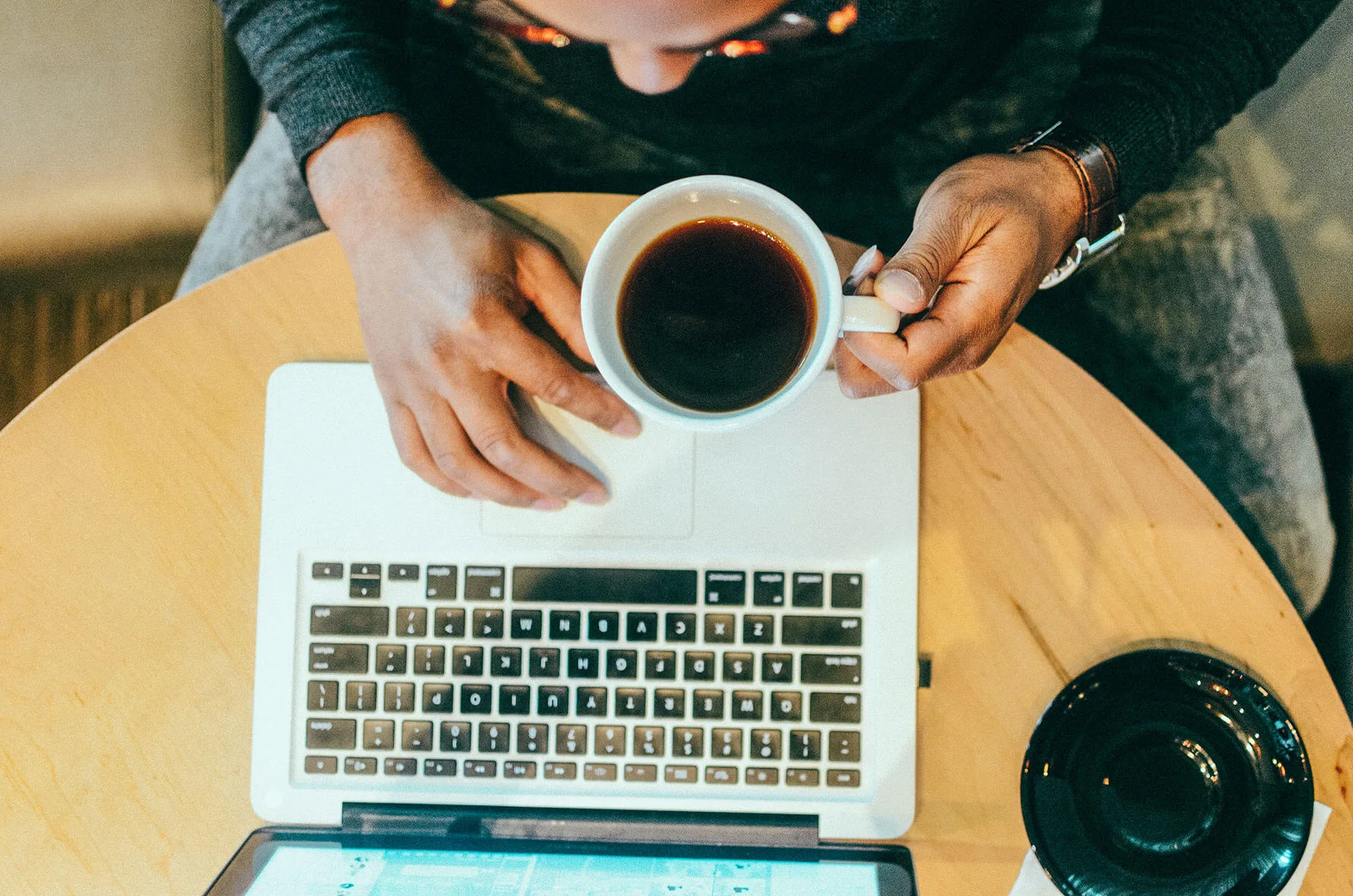 Hands at a laptop with coffee in warm afternoon light.