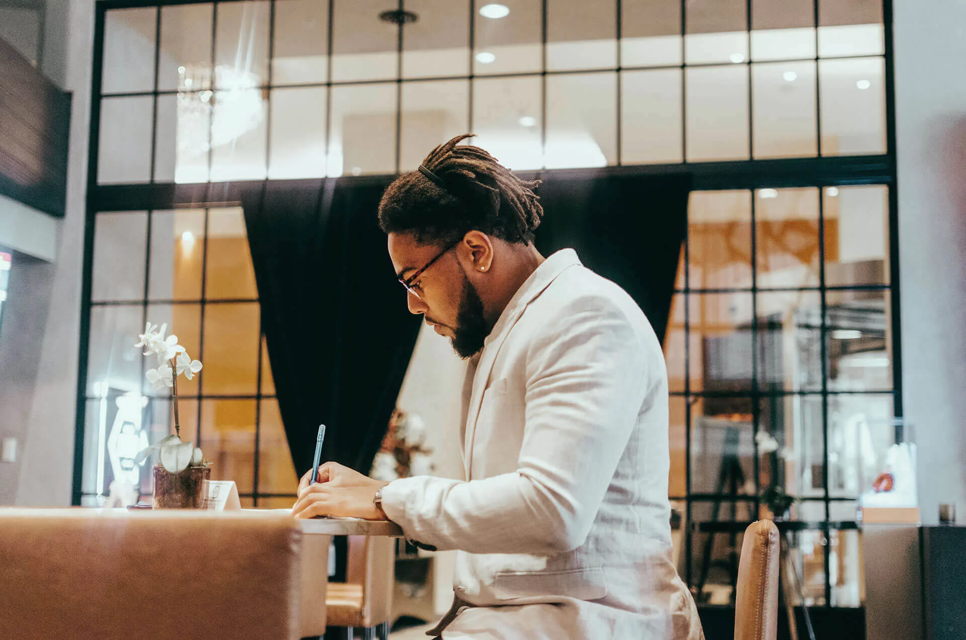 A man in a cream blazer journaling under warm studio light.
